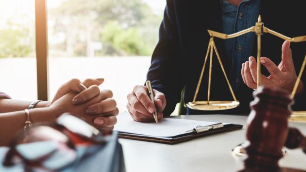 A lawyer sits with a client and reviews paperwork on a clipboard on her desk