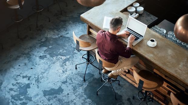 A young professional sits in a coffee shop working on his laptop