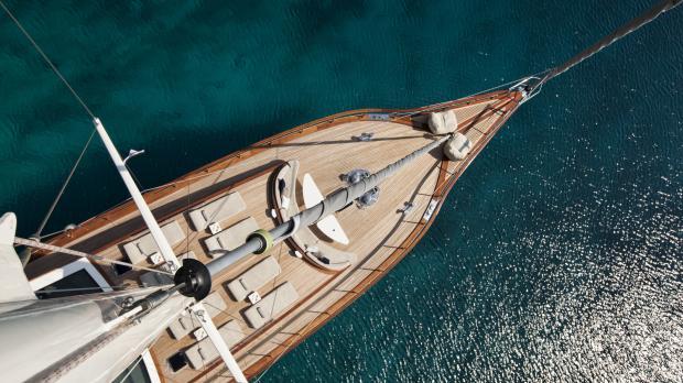 A view from the top of a mast looking down on a luxury yacht sailing in clear waters